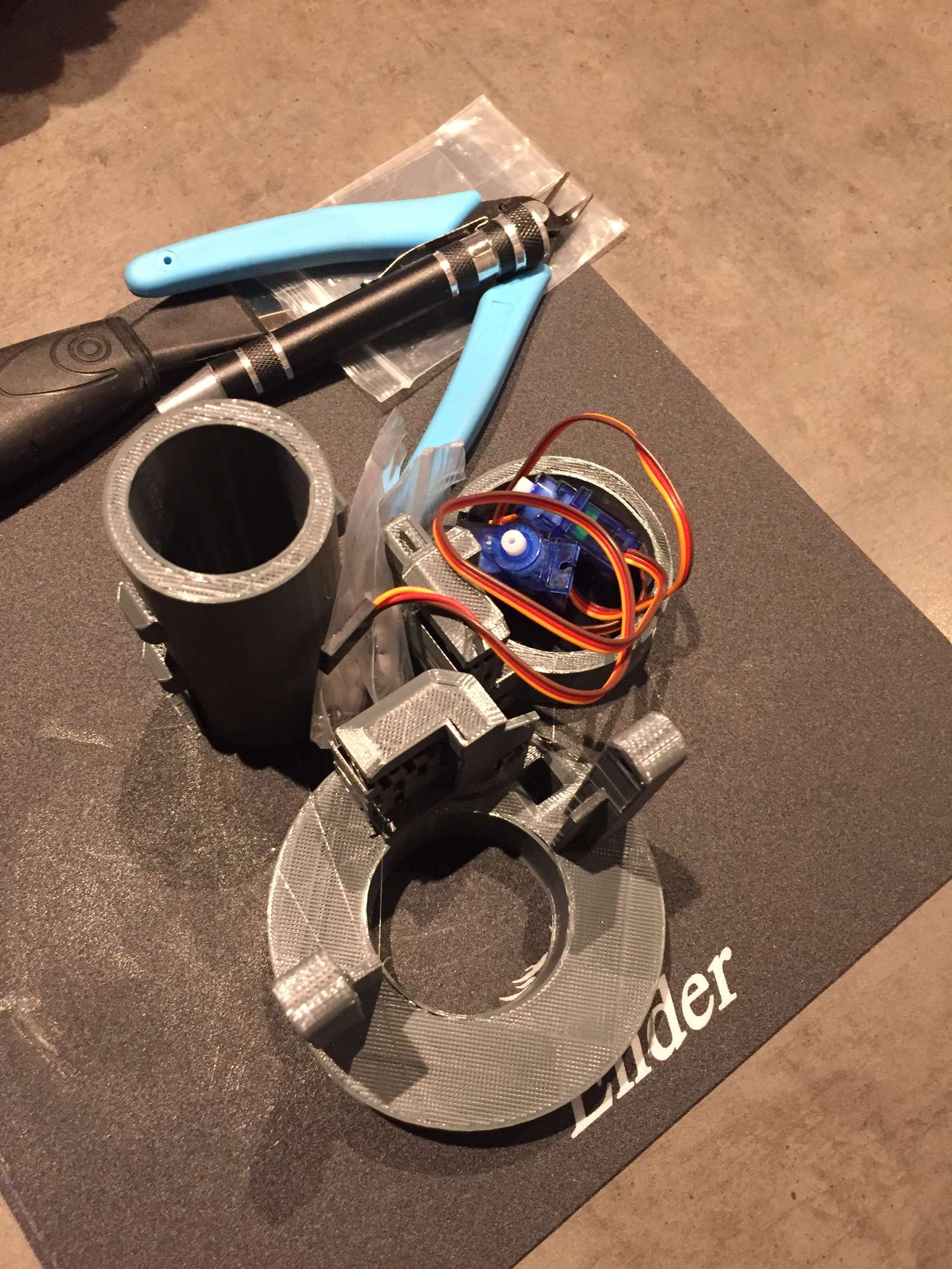 The mk1 gimbal parts and two servos on a cutting mat next to pliers
